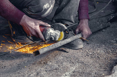 Low section of worker using power tool on metal at workshop