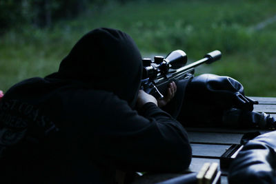 Rear view of man aiming sniper while lying on wooden floor