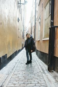 Full length of happy woman standing amidst buildings on alley in city