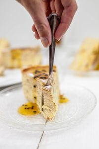 Cropped hand cutting dessert with fork on table