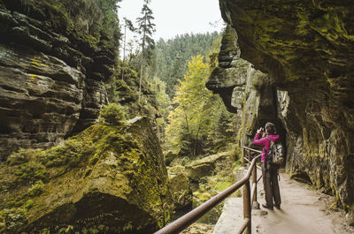 Woman photographing while standing on bridge by cliff