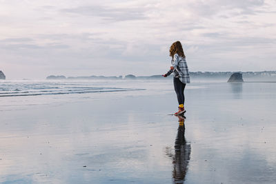 Rear view of woman standing at beach against sky