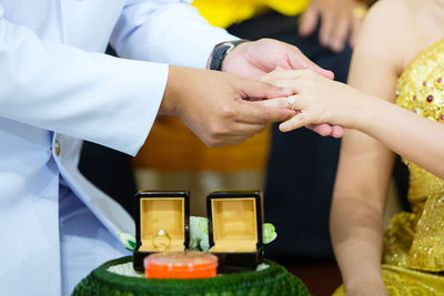 Midsection of bride putting ring on bridegroom during wedding ceremony