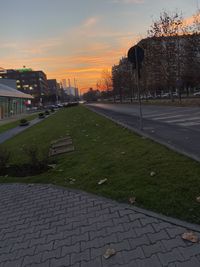 Road by buildings against sky during sunset