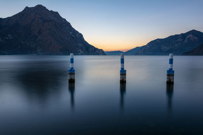 Wooden posts in lake against sky during sunset