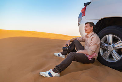 Man sitting on desert against sky