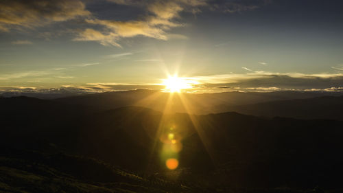 Sunlight streaming through clouds over landscape during sunset