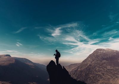 Silhouette man standing on rock against sky