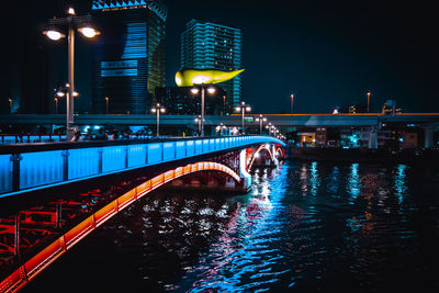 Bridge over river by illuminated buildings in city at night