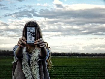 Woman covering face with mirror while standing on grassy field