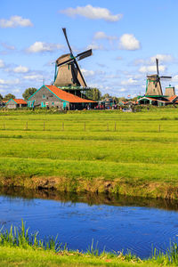 Traditional windmill on field by lake against sky