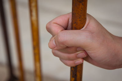 Close-up of man holding rusty prison bars