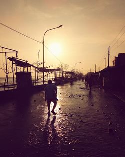 Silhouette man walking on wet city against sky during sunset