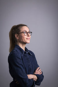 Thoughtful mature businesswoman wearing eyeglasses against gray background