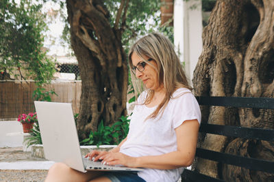 Midsection of woman using mobile phone while sitting on tree trunk