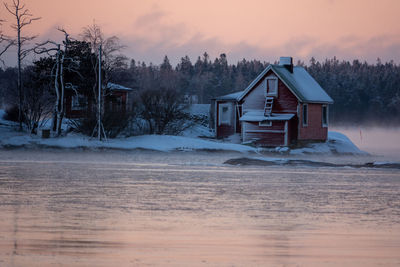 House on snow covered field against sky during sunset