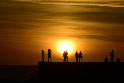 Silhouette people on beach against sky during sunset