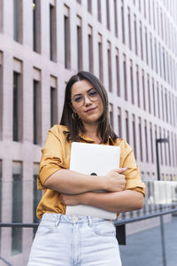 Young businesswoman with laptop standing in office park
