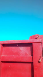 Low angle view of red mailbox on wall against clear blue sky