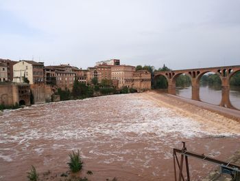 Bridge over river by buildings against sky