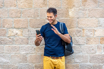 Young man using mobile phone against brick wall