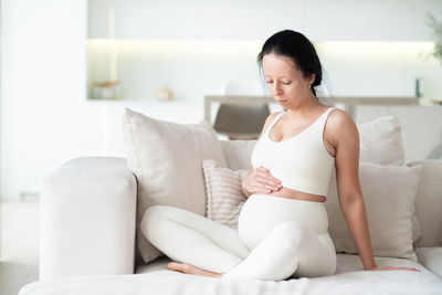 Side view of woman sitting on bed at home