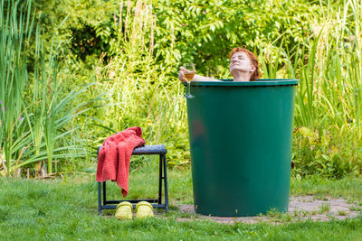 Mature woman with wineglass relaxing in container against plants at yard