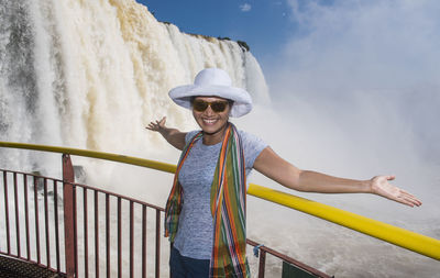 Portrait of smiling woman standing by railing against sky