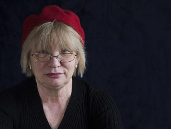 Portrait of mature woman with red cap against black background