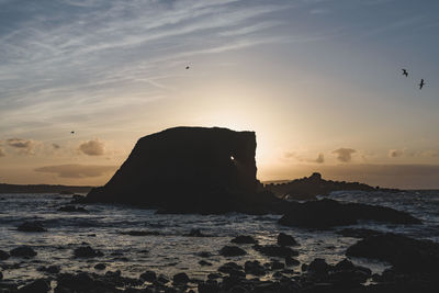 Silhouette rock formation on beach against sky during sunset