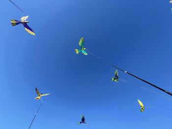 Low angle view of kites flying against clear blue sky