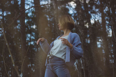 Young woman with short hair dancing against trees in forest