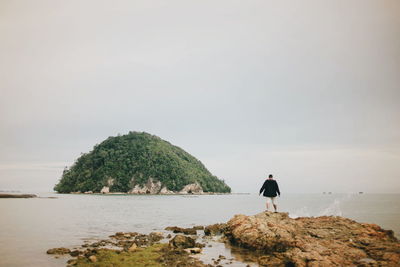 Rear view of man standing on rock against sea