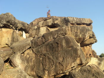 Low angle view of man standing on rock formations against clear sky