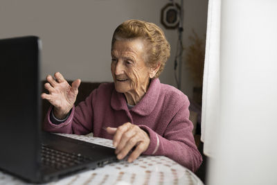 Smiling senior woman having video call on laptop sitting at dining table