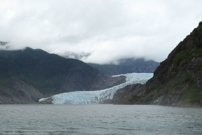 Scenic view of glacier amidst mountains by sea against cloudy sky