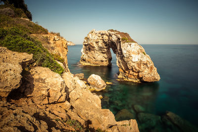 Rock formation in sea against clear sky