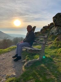 Man sitting on bench against mountains during sunset