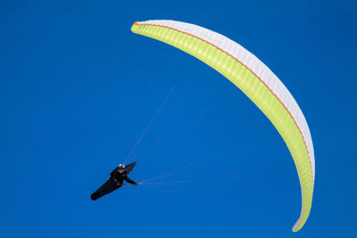 Low angle view of man paragliding against clear blue sky