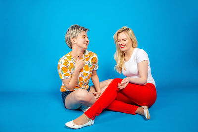 Young woman sitting against blue background