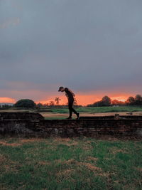 Side view of person standing on field against sky during sunset