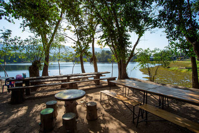 Empty table and chairs by lake against trees