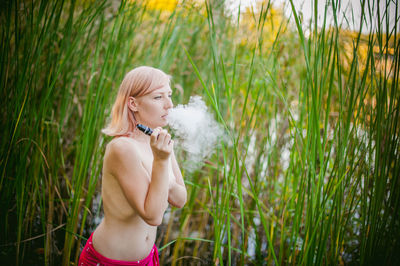 Rear view of shirtless young woman smoking while standing on grassy field