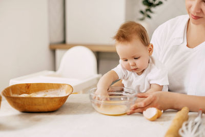 The baby sits in his mother's arms and helps her beat eggs into bowls. new skills, childhood