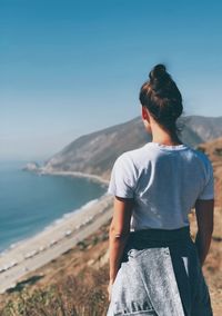 Rear view of woman standing at beach against clear sky