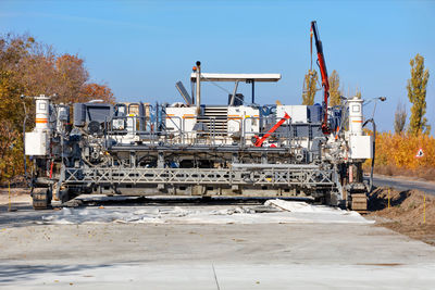 An industrial paver paves a new road on a bright, sunny autumn day.