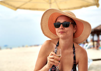 Woman in sun hat and sunglasses holding champagne at beach
