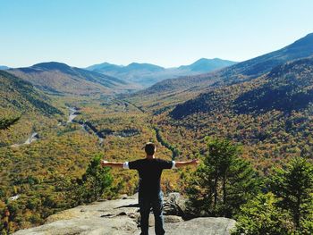 Rear view of man with arms outstretched standing against mountains on sunny day