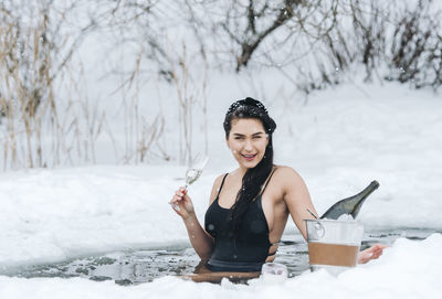 Portrait of smiling woman holding champagne in frozen lake in winter