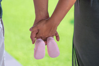 Close-up of couple holding hands with baby booties against field
